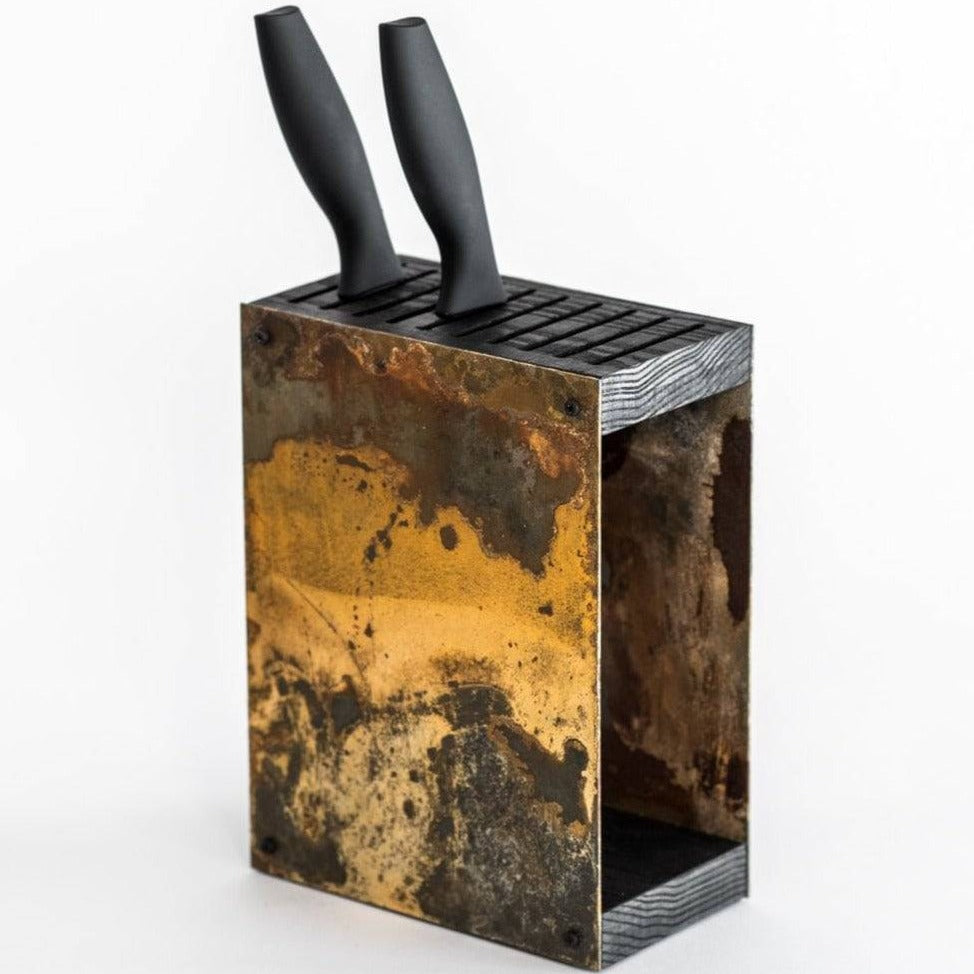 Rustic, industrial-style knife block with a weathered, patina-finished exterior and a wooden top, holding two black-handled knives. The block features a side slot for additional storage and is displayed against a white background.