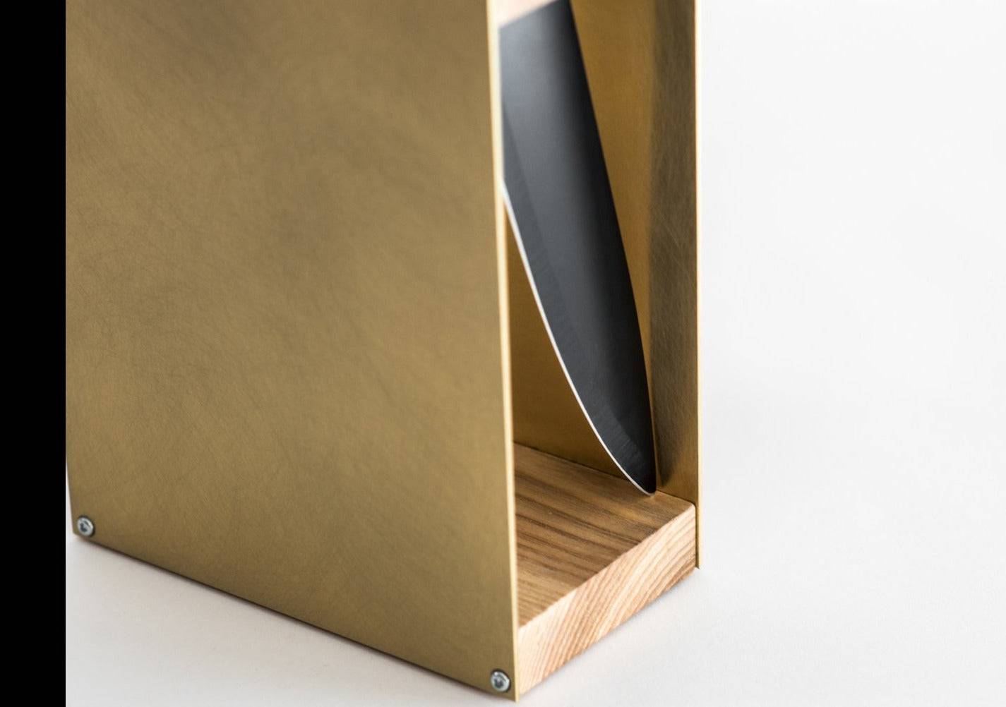 Close-up of a gold knife block with a natural wood base and a visible side slot holding a knife. The smooth wooden grain contrasts with the matte green metal, displayed against a white background.