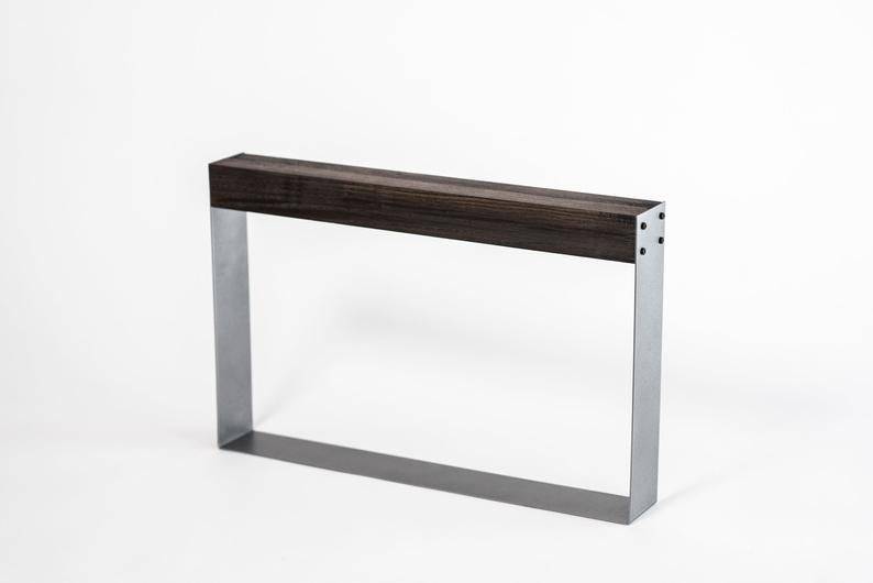 Minimalist knife holder with a dark wooden top and rectangular silver metal frame, featuring exposed black screws on one side, standing empty against a white background.