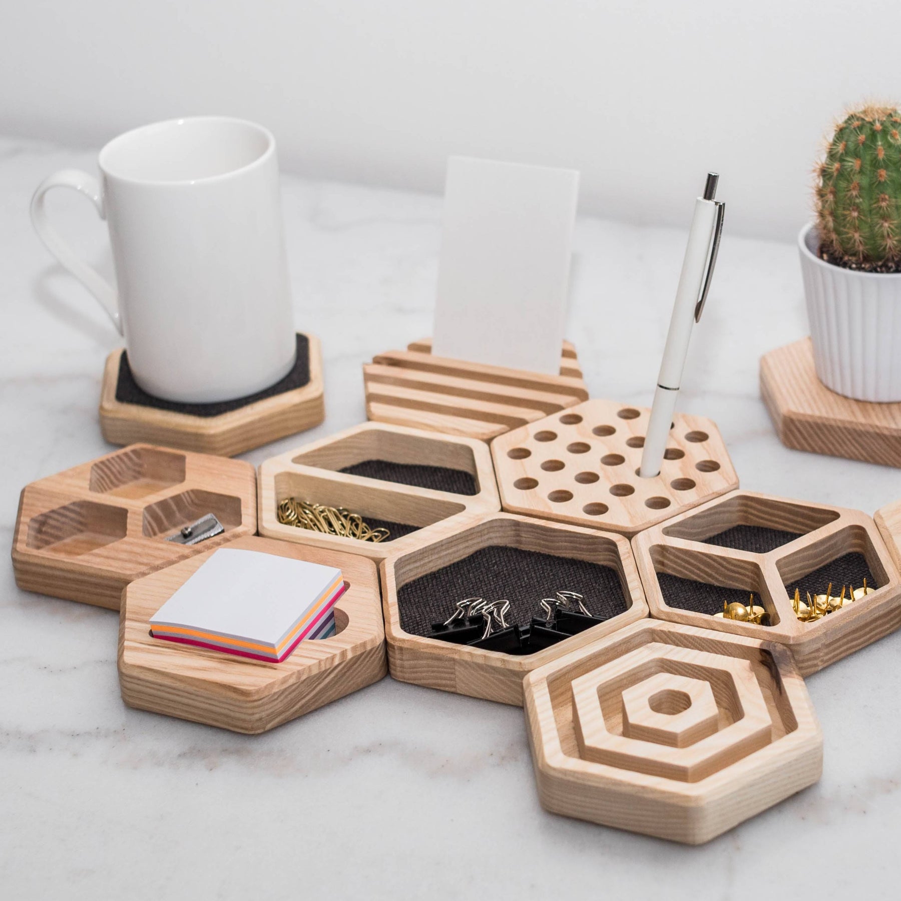 Hexagonal wooden desk organizers arranged neatly, featuring compartments for office supplies like paper clips, thumbtacks, and sticky notes. Includes a coaster holding a mug, a pen holder, and a small cactus planter for added style and functionality.