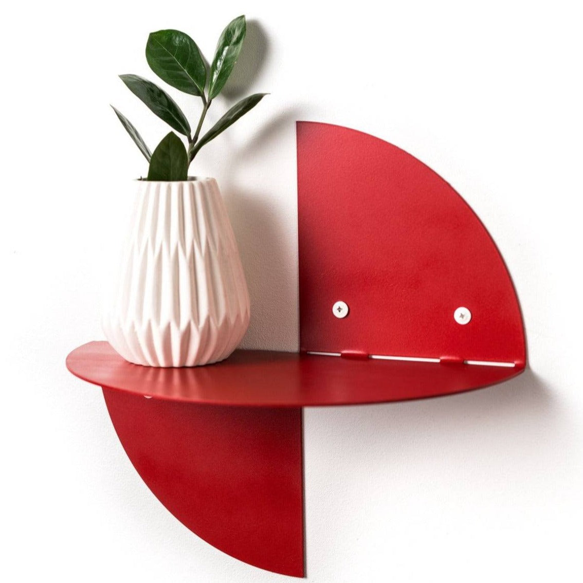 Red half-circle wall shelf with a white vase holding a plant, attached to the wall with visible screws, set against a plain white background.