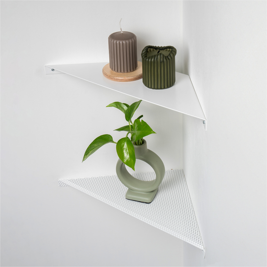 Two white metal corner shelves attached in white corner candles and a plant placed on the shelves