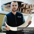 A craftsman from EWART WOODS holding a curved piece of wood, showcasing skilled craftsmanship in the workshop.
