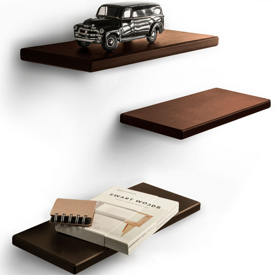 Three floating rectangular shelves stained in dark brown with smooth edges and wood grain texture. The top shelf holds a vintage car model, and the bottom shelf has a notebook and a book.