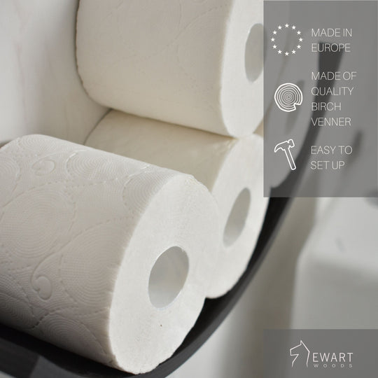 Close-up of three toilet paper rolls displayed on a curved wooden holder. The image includes text highlighting that the product is made in Europe, made of quality birch veneer, and easy to set up. The EWART WOODS logo is visible.