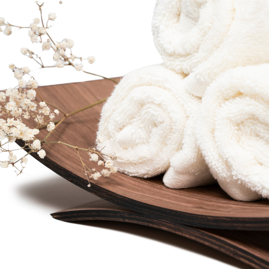 Curved wooden holder with rolled white towels and decorative white flowers, isolated on a white background.