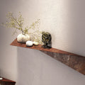 Rustic metal decor shelf with an angular design, holding a decorative plant in a white pot, two smooth stones, and a black statue, set against a textured wall.