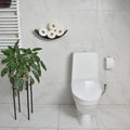 Front view of dark wood curved toilet paper holder mounted on a bathroom wall, displaying four rolls of toilet paper. The bathroom features minimalist design with a plant, modern fixtures, and a clean, marble tile backdrop.