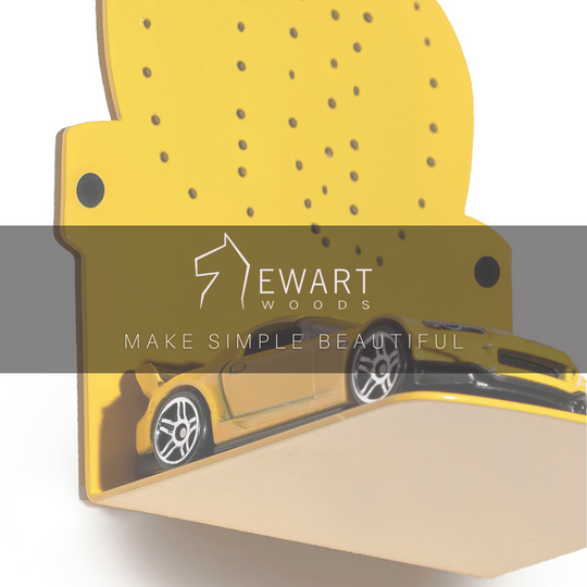 Close-up of a yellow perforated metal wall shelf in a cactus shape, holding a small toy car, with the brand slogan &