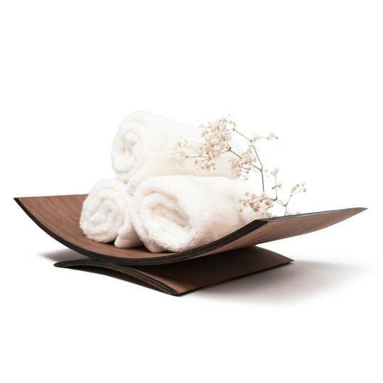 Curved wooden holder with rolled white towels and decorative white flowers, isolated on a white background.