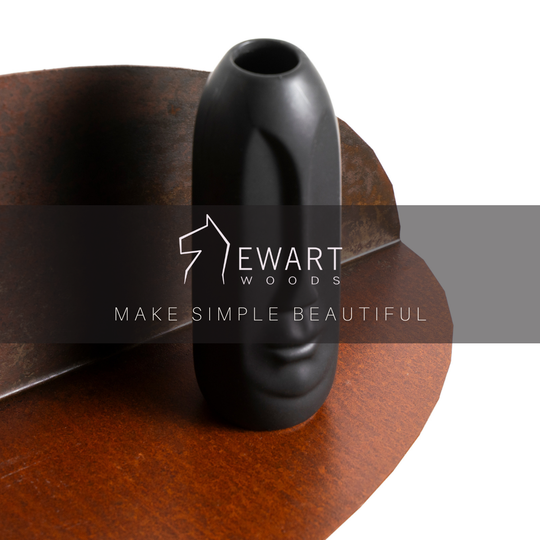 Black decorative moai statue on a curved metal shelf with a rustic, oxidized finish. The image features the &