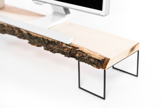 Computer monitor on a live-edge wood stand with an organic bark finish, supported by sleek black metal frame legs.