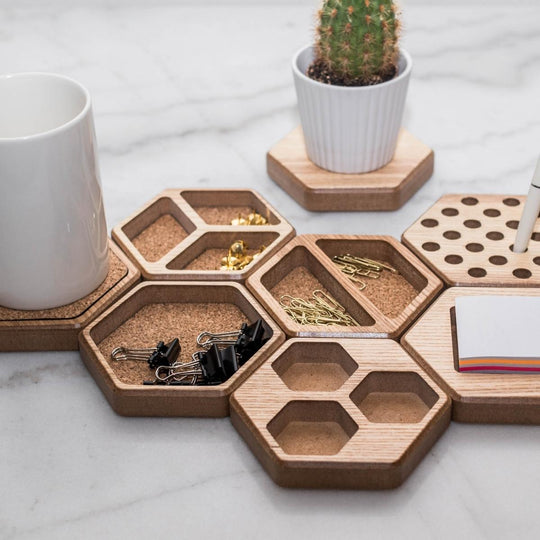 Hexagonal wooden desk organizers arranged on a marble surface, holding paper clips, binder clips, sticky notes, a mug, and a small potted cactus.