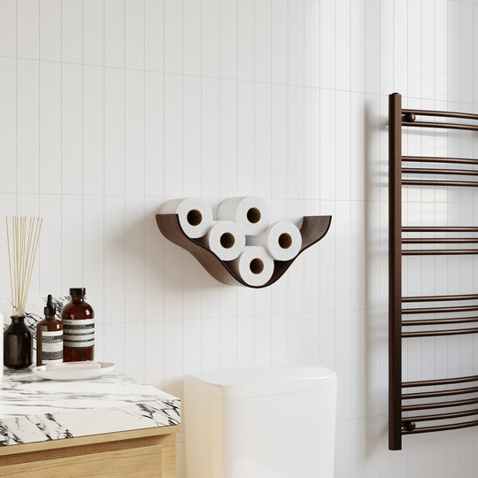 Walnut wooden wall shelf with a cloud-like, curved design holding five rolls of toilet paper, mounted on white tiled walls in a modern bathroom next to a toilet and towel rack.