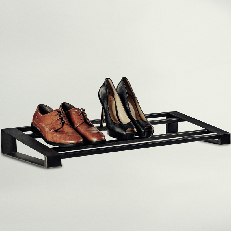A black metal shoe rack holding a pair of brown leather lace-up oxford shoes and a pair of black high-heeled pumps, photographed against a clean light gray studio background.
