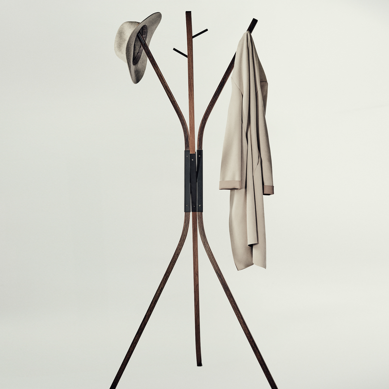A modern wooden coat rack with three legs and curved top arms, shown against a plain light gray background. A hat is hanging on the left hook and a light beige coat is hanging on the right.