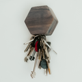 A hexagonal grey wooden key holder mounted on a wall, holding a set of metal keys on a keyring.