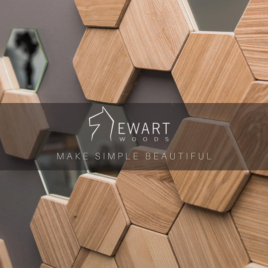 Close-up of hexagonal wooden tiles and mirror pieces arranged on a gray wall, featuring the Ewart Woods logo with the tagline &