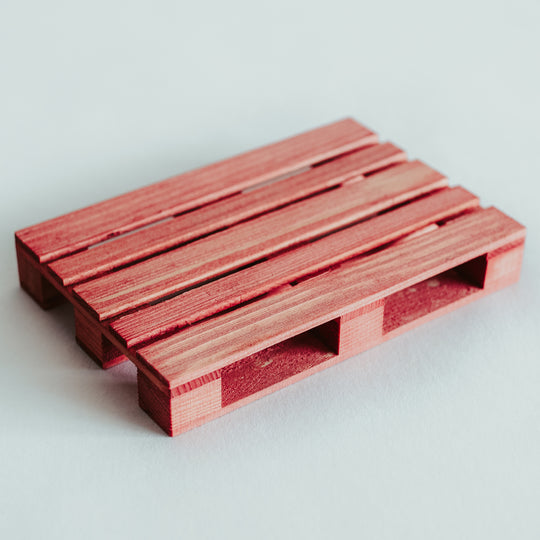 Handmade wooden pallet coaster in a vibrant red stain, featuring smooth, polished slats and carefully crafted details, resting on a white surface.