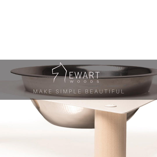 Close-up of a raised pet feeder with a stainless steel bowl in a triangular metal top, supported by wooden legs, with Ewart Woods branding.