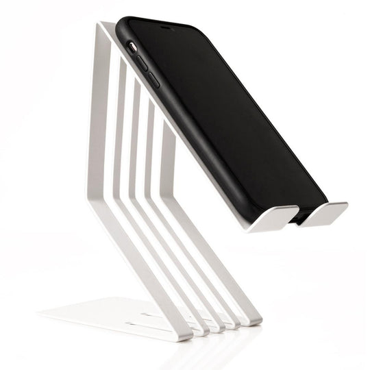A smartphone resting on a white metal phone holder with a unique slatted design and an integrated charging slot, angled for easy viewing.