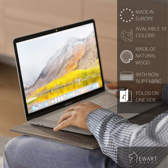 A person using a laptop on a wooden sofa tray. Features: Made in Europe, 10 color options, natural wood, non-slip fabric, folds on one side. Ewart Woods logo is visible in the corner.