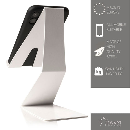White Z-shaped phone stand holding a smartphone, with product details on the right mentioning European-made, all-mobile compatibility, high-quality steel, and 1kg capacity.