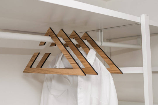 Set of wooden hangers in paldau finish, featuring a geometric triangular design with a smooth yet textured surface, holding white shirts on a closet rod.