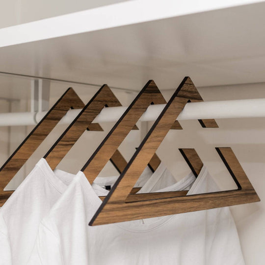 Stylish wooden hangers with a geometric triangular design, showcasing a rich paldau  finish. The hangers hold white t-shirts in a minimalist closet setup.