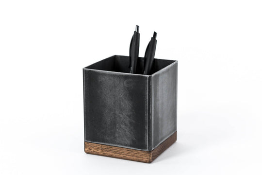 Black metal pen holder with a distressed texture and wooden base, holding black pens.