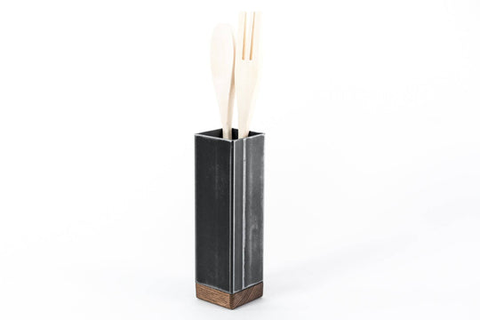 Black metal utensil holder with a wooden base and wooden utensils.