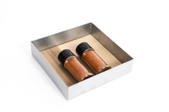Square metal tray with a wooden base, containing two glass spice bottles filled with red spices.