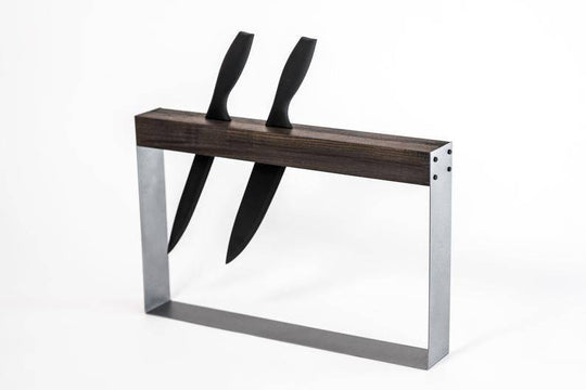 A modern, minimalist knife holder with two black-handled knives inserted vertically into a rectangular wooden and metal frame, designed for easy access and storage.