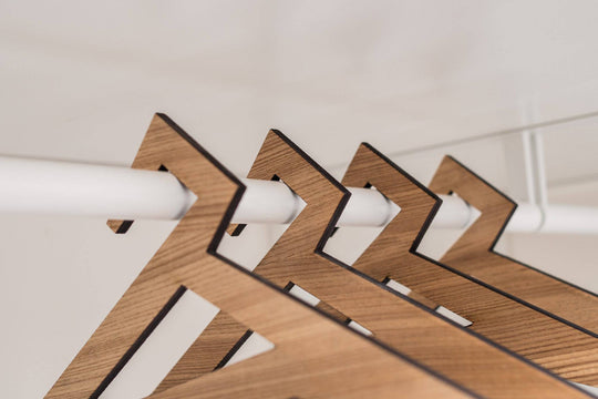 Close-up of wooden hangers in paldau finish with a geometric triangular design, hanging on a closet rod.
