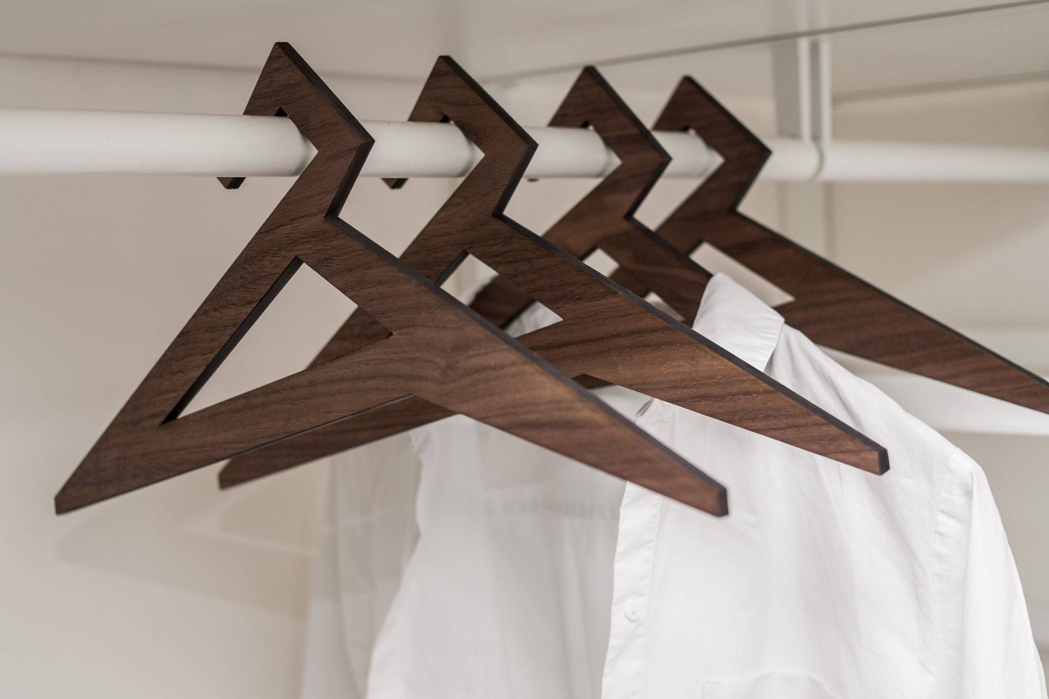 Geometric wooden hangers with a triangular design and rich walnut finish, holding a white shirt in a minimalist closet.