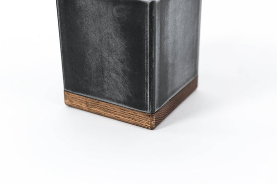 Close-up of a black metal container with a slightly distressed texture and a wooden base.