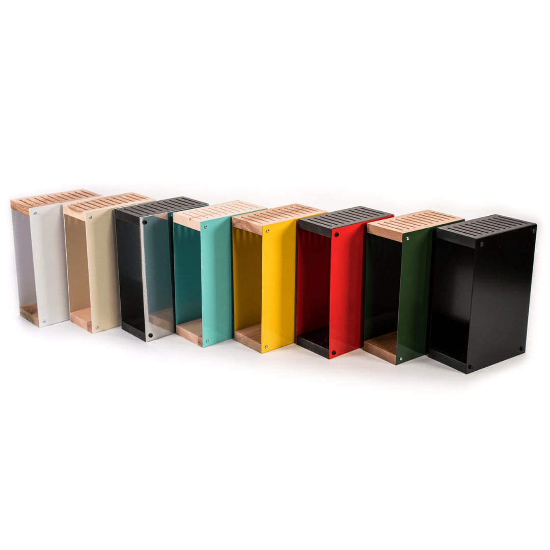 Lineup of colorful knife blocks in various shades, including gray, beige, black, teal, yellow, red, and green. Each block features a wooden top and base, arranged in a gradient pattern and displayed against a white background.