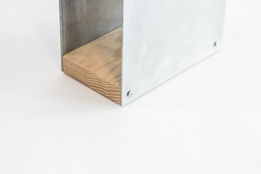 Close-up of a metal knife block with a smooth silver finish and a natural wood base. The block is displayed against a plain white background, showing the wooden grain detail at the bottom.