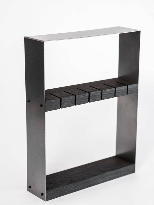 Angled view of an industrial-style knife holder featuring a dark wood block and a rugged matte black metal frame, with precision-cut horizontal slots for knife storage, set against a white background.