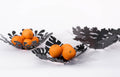 Three black metal bowls with intricate leaf cutout designs, two holding vibrant oranges, displayed in a sleek, contemporary style.