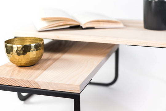 Close-up of a contemporary home decor piece: an industrial-style wood and metal side table with two levels, featuring a gold bowl and an open book.