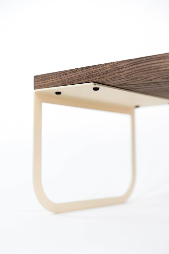 Close-up view of the underside of a minimalist tray, showing black screws securing the dark wooden surface to the light-colored metal leg, set against a white background.