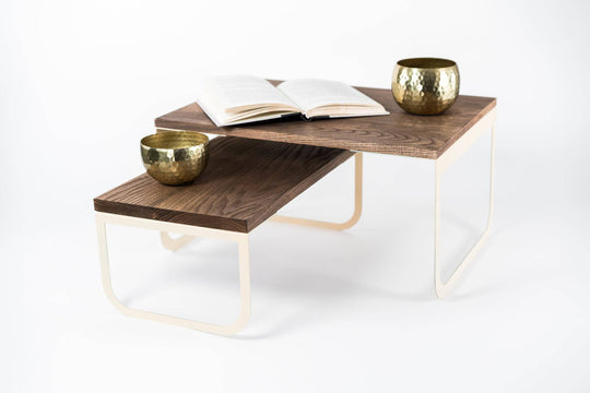 Two-tier wooden tray with light-colored metal legs, an open book, and two brass bowls, set against a white background.