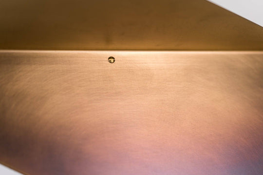 Close-up of the brushed copper finish on a triangular shelf, with a visible screw securing it to the wall.