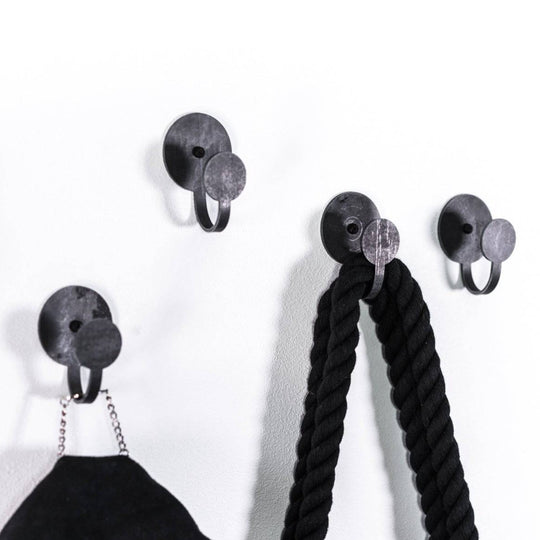 Set of three black metal wall hooks with circular design, each holding accessories like ropes and bags, adding a minimalist industrial touch to the wall.