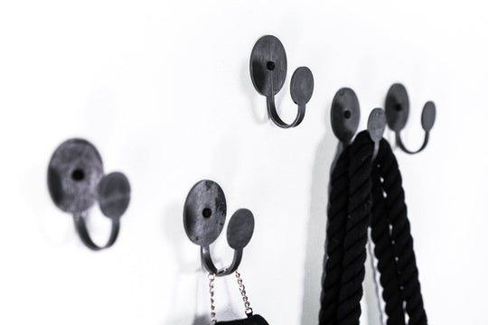Black metal wall hooks with round bases, designed to hold ropes, bags, and accessories, showcasing a sleek and modern look.