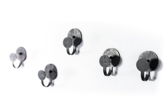 Five black metal hooks with textured finishes, featuring round backplates and rings, arranged on a wall in a minimalist, industrial style.