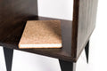 Close-up of the open compartment in a dark-stained wooden side table, showcasing a cork-covered notebook placed on the shelf.