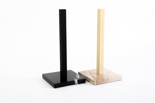 Two paper towel holders with marble bases: one in black marble with a black metal stand, and the other in beige marble with a gold metal stand, combining functionality with timeless style.