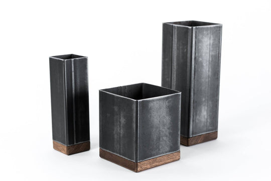 Set of three black metal utensil holders with wooden bases in different heights, in an industrial style.